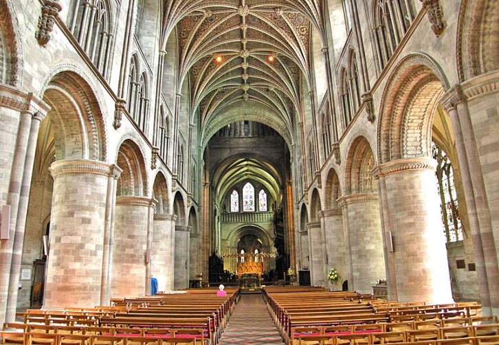 The nave of Hereford Cathedral showing the rounded arches of the Norman period above which are the pointed arches and elaborate rib vaulting of 14th century Gothic. 